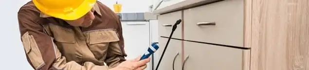 Roach exterminator applying treatment under kitchen cabinets in Cape Coral, FL