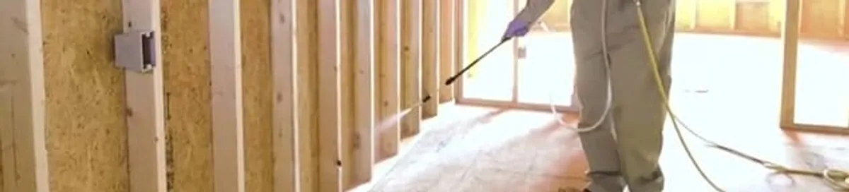 Termite treatment technician applying spray along framing and unfinished walls in Cape Coral, FL