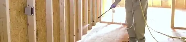 Termite treatment technician applying spray along framing and unfinished walls in Cape Coral, FL